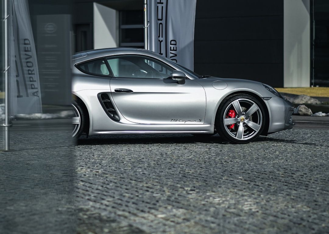 203 Porsche Cayman S in silver, parked on concrete near a Porsche retailer store with “ADVclientId Julien” written next to it. Shot in the style of canon eos r5, wide angle shot, high resolution photography. –ar 128:91