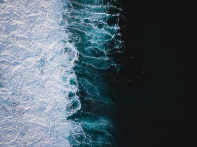 aerial view of ocean waves on the left side and black water on right, high resolution photography, professional color grading, no contrast, clean sharp focus, no grainy textures, cinematic photography, unsplash style --ar 128:95