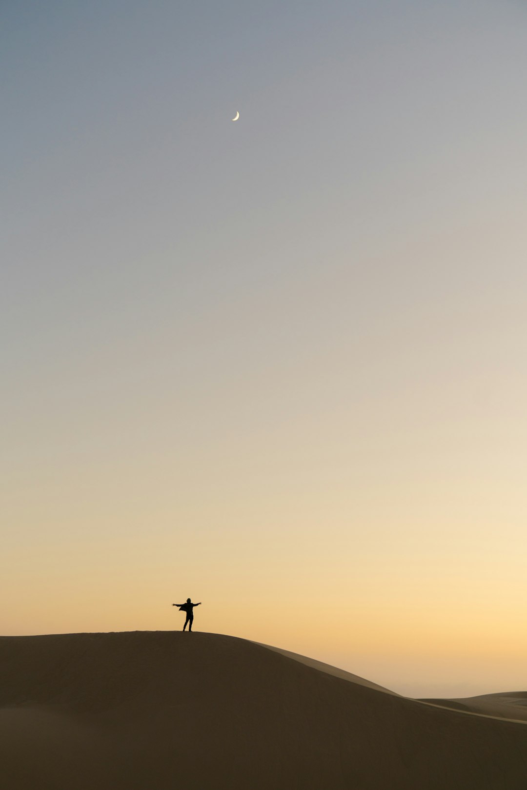 A lone dancer on the top of sand dune at dawn, with clear sky and crescent moon in background, symbolizing solitude and self vwew, minimalist photography style, soft lighting, wideangle lens, neutral tones, serene atmosphere, tranquil mood. –ar 85:128