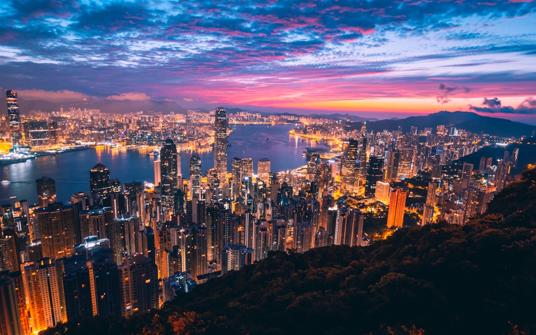 A breathtaking view of Hong Kong at night, showcasing the city’s vibrant lights and skyscrapers from atop victoria mountain overlooking hong k.setImageBitmap nails and holographic water in the background. The sky is painted with hues of pink blue purple as the sun sets behind the mountains, casting long shadows over buildings and creating an enchanting atmosphere. In closeup shot, a couple stands handinhand enjoying the stunning panoramic view of cityscape. –ar 8:5