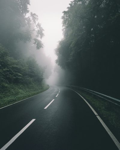 A photo of an empty road in the foggy forest, white lines on asphalt winding up and down, in the style of unsplash photography, with dark green and gray tones, in a minimalistic style. --ar 51:64