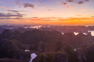 The view of Ha Long Bay from above was spectacular, with a sunrise over an endless sea of islands and rocks. The colors in the sky captured a golden hue, creating a beautiful contrast with the green mountains below. A drone captured the scene from above, showcasing the vastness of nature's creation. --ar 128:85