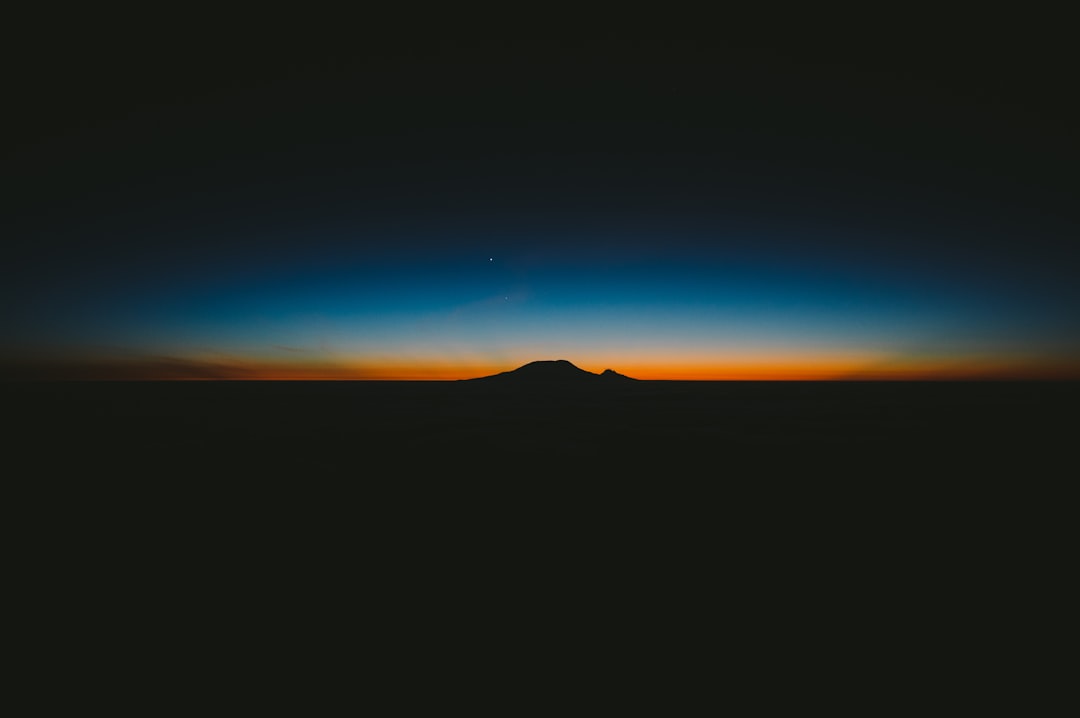 Silhouette of Mount Fuji in the distance at night, clear sky, blue and orange gradient sky, horizon, shot from above, minimalism, photography, black background, no clouds, Sony Alpha A7 III, Sony FE2485mm f/30 mm g master lens, f/6.9, ISO 200, 1/60s shutter speed, low key, sunset in the style of minimalism. –ar 128:85