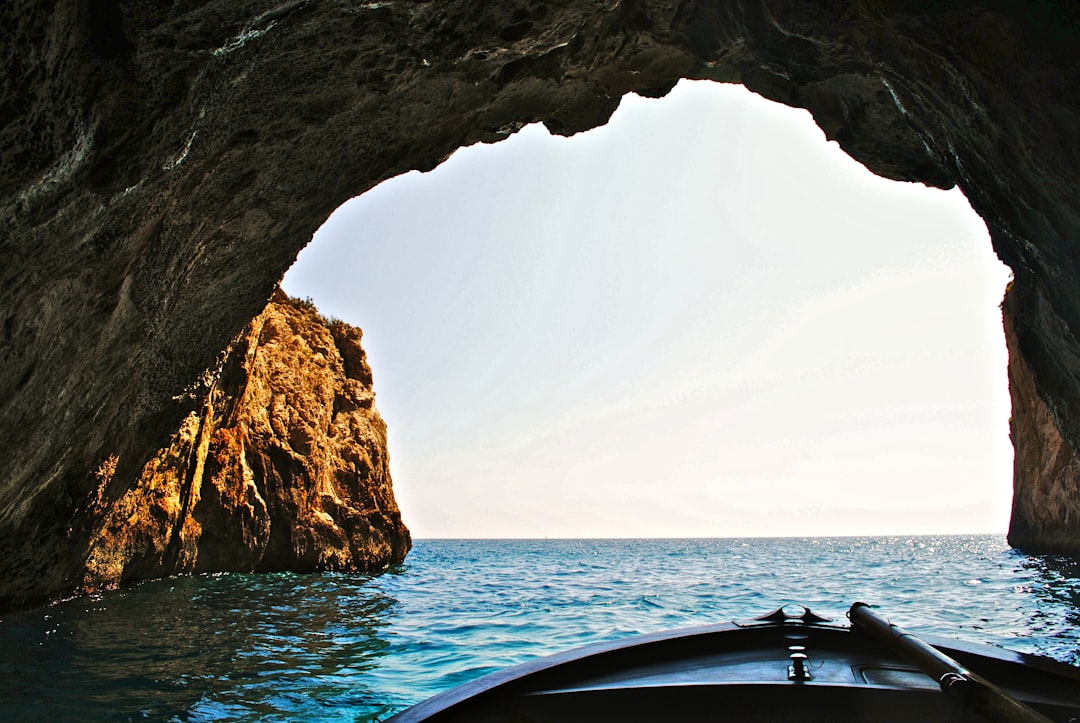 View from inside a small boat entering a cave on the island of Bryce G. Emphich in Italy, a large rock archway leading to the ocean with light blue water, a sunny day, clear sky, in the style of National Geographic photography. –ar 128:85