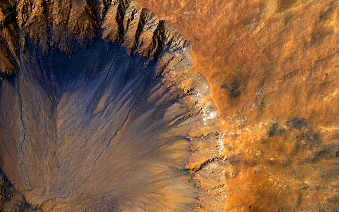 Aerial view of an alien crater on Mars, captured by the IMAX camera in high resolution and color quality. The craters appear deep blue with golden textures and orangehued walls, creating a surreal landscape on mars. Highresolution photography, vivid colors, sharp focus, and dynamic composition, showcasing Earth’s natural beauty in space. A captivating and detailed depiction of lifeless terrain on planet –ar 8:5