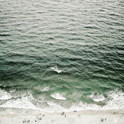 photo of ocean from above, waves with people swimming in the water, minimalist style, green and gray tones, natural light, calm atmosphere, bird's eye view, wide lens perspective, people on the beach below.