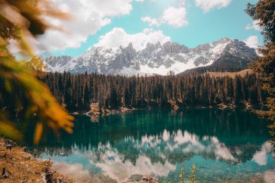 A picturesque view of the Dolomites in Italy, with clear blue waters reflecting snowcapped peaks and lush green forests surrounding an emerald lake. In the style of unsplash photography, high resolution. --ar 128:85