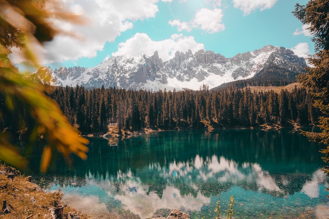 A picturesque view of the Dolomites in Italy, with clear blue waters reflecting snowcapped peaks and lush green forests surrounding an emerald lake. In the style of unsplash photography, high resolution. –ar 128:85