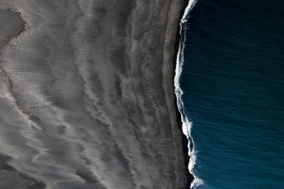 aerial view of black sand beach, ocean waves, drone photography, minimalist, dark blue and gray tones --ar 128:85