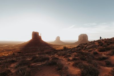 A photo of the desert landscape with two rock formations in Monument Valley, soft light, minimal, vastness, golden hour, a lone biker riding down the horizon in the style of unsplash photography. --ar 128:85