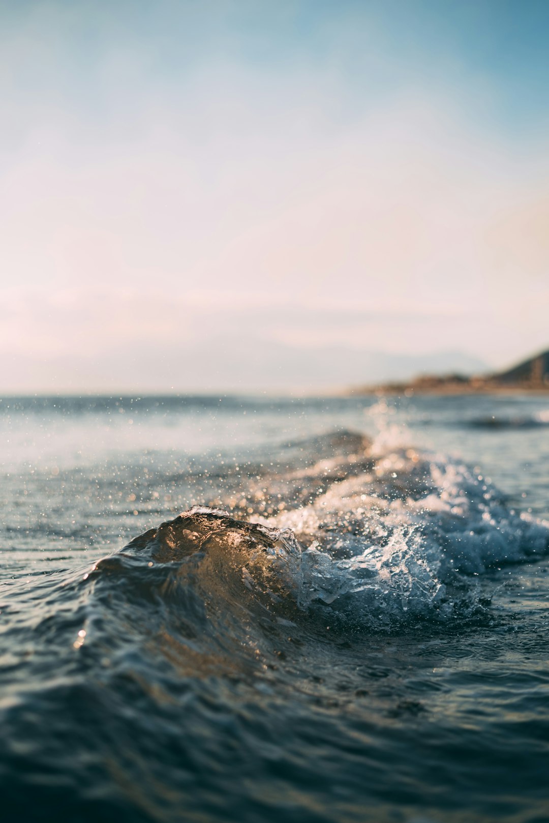 photograph of a small wave in the ocean, on a beach, with the sky, in daylight, during summer, with a shallow depth of field, with a blurred background, in the style of unsplash photography. –ar 85:128