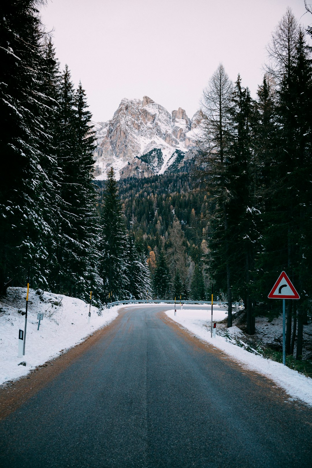 photo of an Italian road in the Dolomites, with snow on the ground and trees, a traffic sign visible on the right side, in the style of unsplash photography –ar 85:128