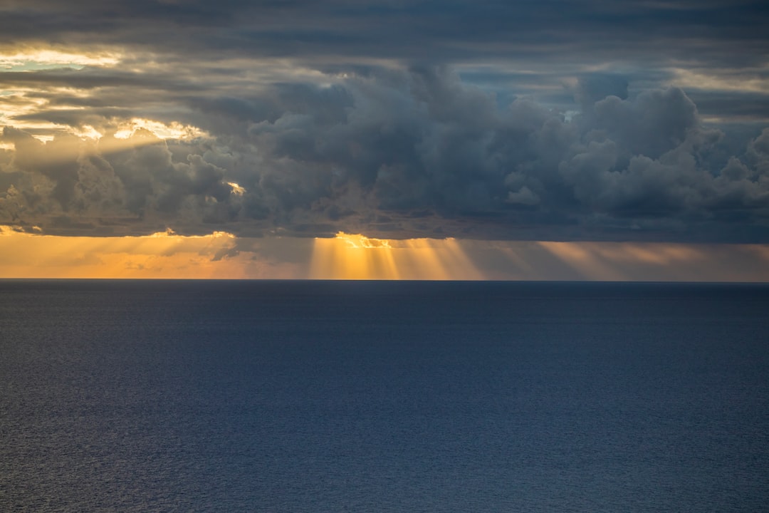 Sun rays breaking through dark clouds over the ocean, seen from above. Shot in the style of Nikon D850 with an 2470mm f/3 lens at ISO. –ar 128:85