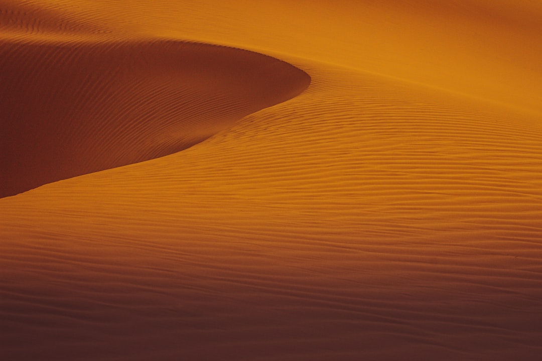 A photo of the Sahara Desert, capturing the intricate patterns and textures in golden sand dunes under soft sunset lighting. The scene is minimalist with high contrast between warm tones of orange to grey. The focus on texture adds depth and detail to the vastness of desert landscapes. –ar 128:85