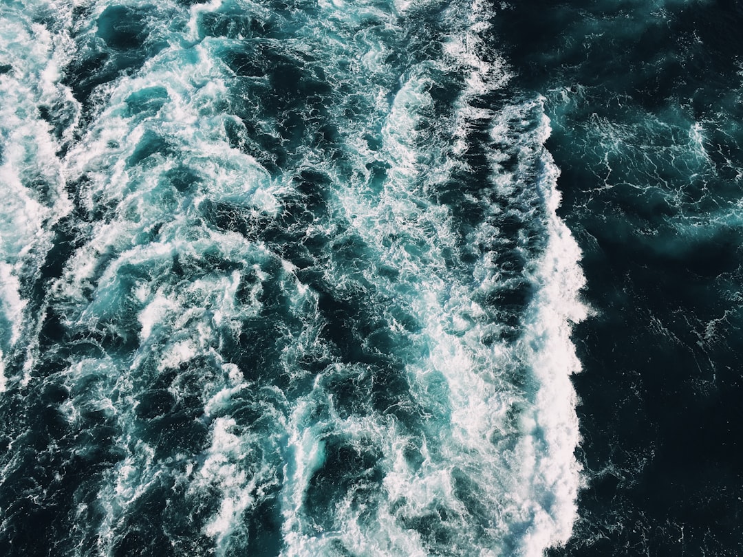 Aerial view of ocean waves in the style of dark blue and white, aerial photography from a top down perspective in dark green and light black, detailed texture, using a Fujifilm Pro400H film, from a bird’s eye angle with a diagonal composition, sharp focus, high resolution, hyperrealistic style, with a wideangle lens, natural lighting, soft shadowing, depth of field. The sea is full of water splashes. Water drops are visible on the camera glass, the photo taken with a Sony Alpha A7 III. –ar 4:3