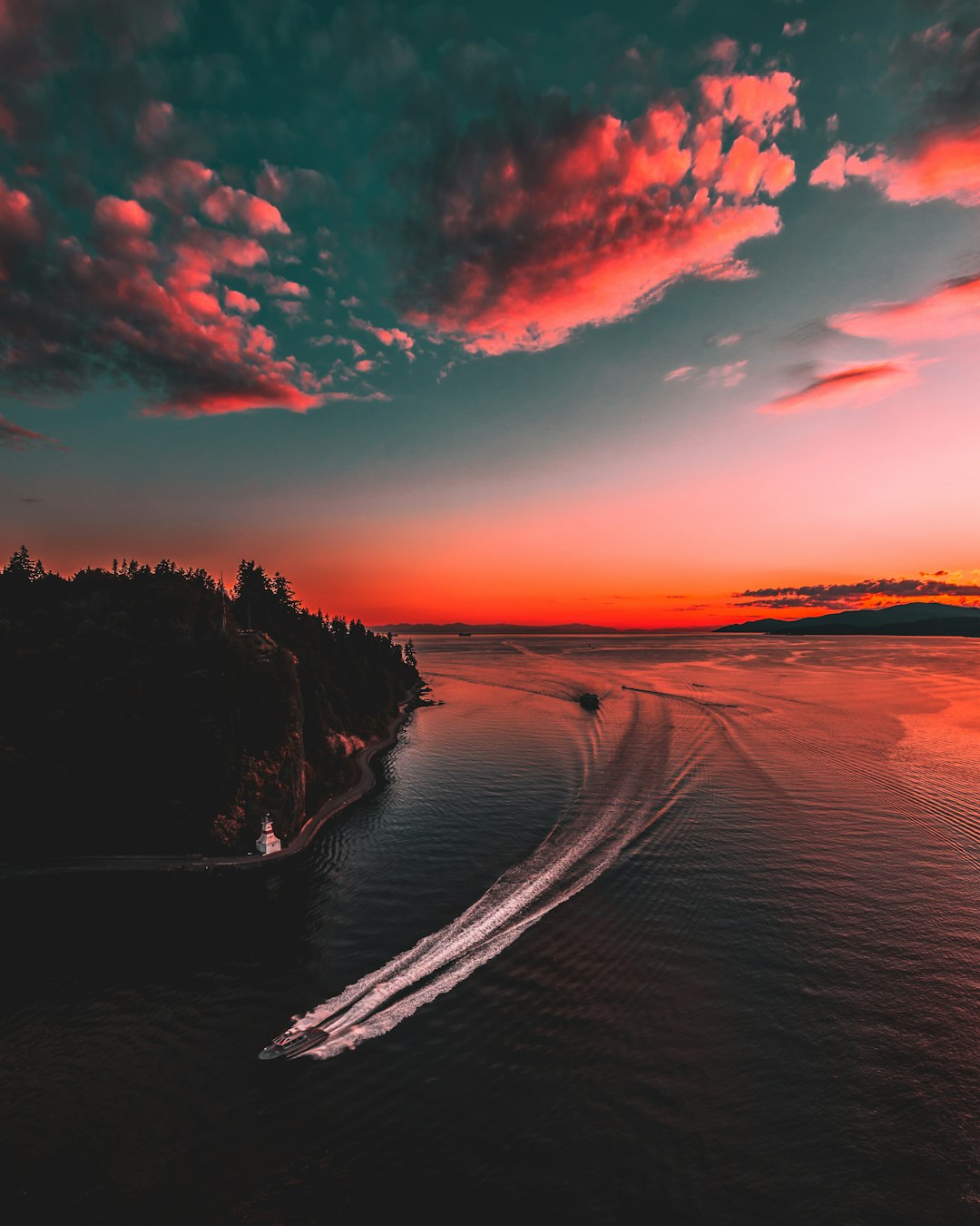 A boat driving on the sea, sunset sky, silhouette of red clouds, aerial view, high angle shot, drone perspective, coastline, dark pink and orange tones, distant islands, buildings, lush forests, water flow. Realistic photography style, wideangle lens, bright colors, soft lighting, capturing the dynamic speed. High resolution, full details, high definition, in the style of a realistic photographer. –ar 51:64