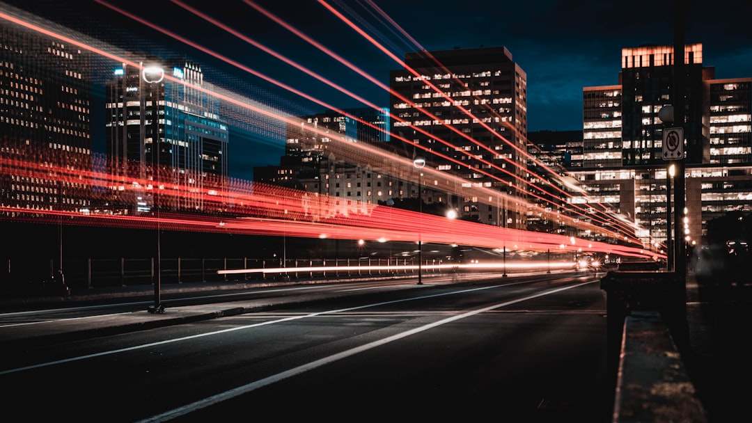 A long exposure photograph of city lights and traffic on the streets at night, creating streaks that form an abstract pattern in red and white. The focus is sharp with light trails from cars moving past. In the background buildings glow against the dark sky. Shot in the style of Canon EOS R5 at F2 ISO30. –ar 16:9