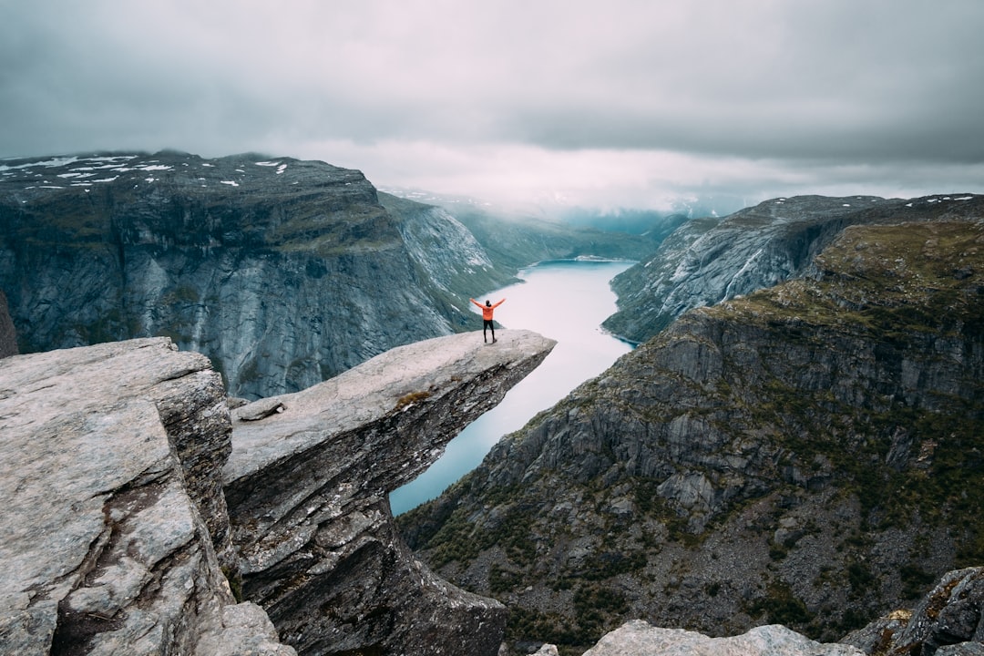 photo of an adventurous woman standing on the edge overlooking dramatic mountains and rivers in Norway’s fjords, wide angle shot, in the style of unsplash photography. –ar 128:85