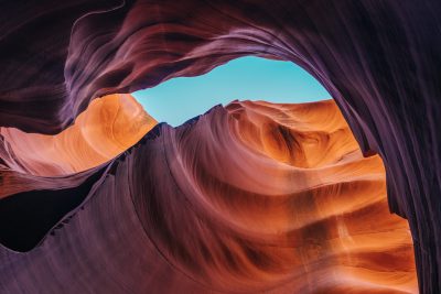 A stunning photo of an orange and purple sandstone canyon in the Arizona desert, taken from inside with a wideangle lens. The sky is clear blue above. A deep black hole appears at one end of the composition, adding depth to the scene. This photograph was captured using Sony Alpha III. --ar 128:85