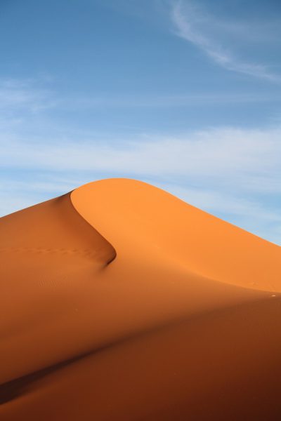 photograph of the top half of an orange sand dune, blue sky, realistic, shot in the style of canon eos r5 --ar 85:128