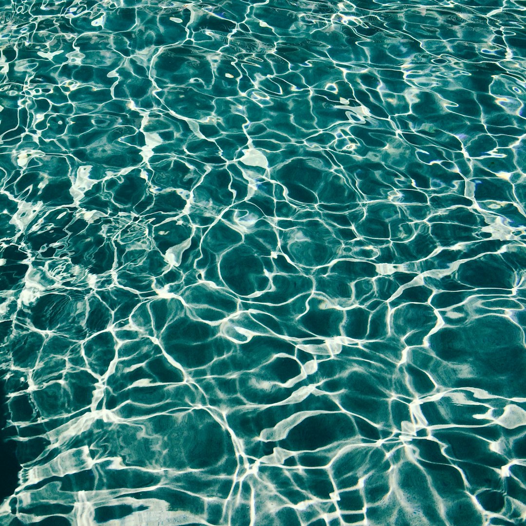 A photograph of clear teal water in the pool. Light and shadow create ripples on the surface, reflections, beautiful in the style of nature.