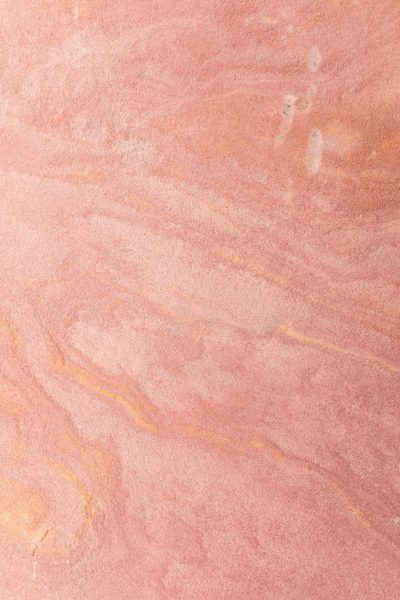 A closeup of the surface texture of pink sandstone, showcasing its unique patterns and colors. The background is plain with no additional elements to highlight the natural beauty of the stone. This photograph was taken by professional photographers using advanced equipment for highly detailed and sharp images. --ar 85:128