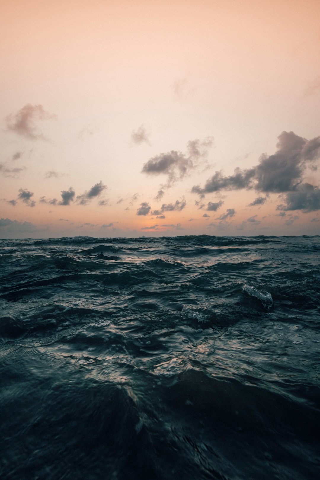 a photo of the ocean at dusk, with a pink and orange sky, soft clouds in the background, gentle waves in front, dark grey water, taken from an underwater camera angle, close up shot, grainy film effect, moody aesthetic, cinematic photography style, depth of field, natural lighting, –ar 85:128