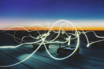 a long exposure photo of light painting in the shape of multiple swirls on top of an empty rooftop at night, horizon with orange and blue sky, concrete floors, black metal furniture --ar 128:85