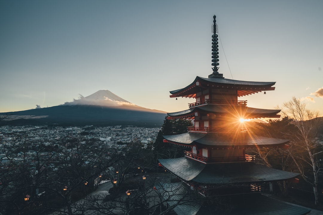 Cinematic photography of Chureito Pagoda with Mount Fuji in the background at sunrise, showcasing beautiful architecture and stunning natural scenery. The sun is rising behind Mount Fuji casting long shadows over the cityscape below. Shot on a Canon EOS R5 camera with a wide-angle lens in the style of landscape photography. –ar 128:85