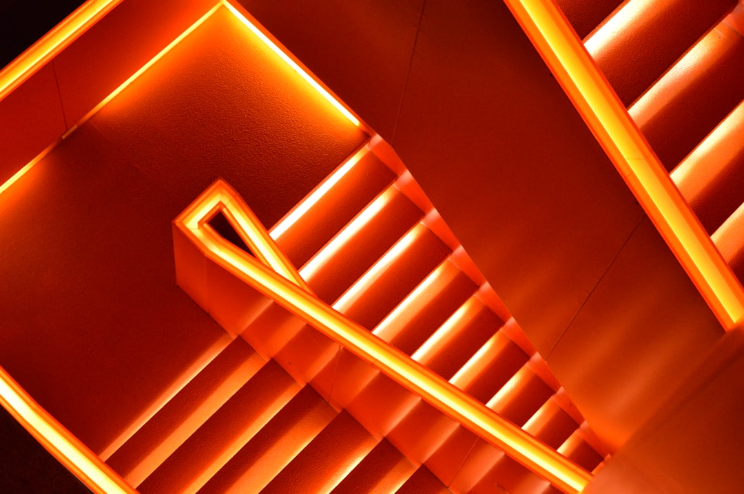 A photo of an orange neon light in the shape of a staircase, depicting modern architecture in a high angle shot with warm lighting and an orange color scheme, presented as a closeup in the style of hyperrealistic art. –ar 128:85