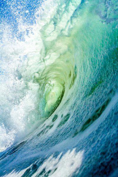 A close-up photo of the inside wall and water spray from an extremely large wave in Hawaii. The shot is taken at ground level looking straight down into the barrel with blue sky above. The color palette is vibrant and beautiful with blues, greens, and whites. The vibe is edgy and intense in the style of a photographer capturing the raw power of nature. --ar 85:128