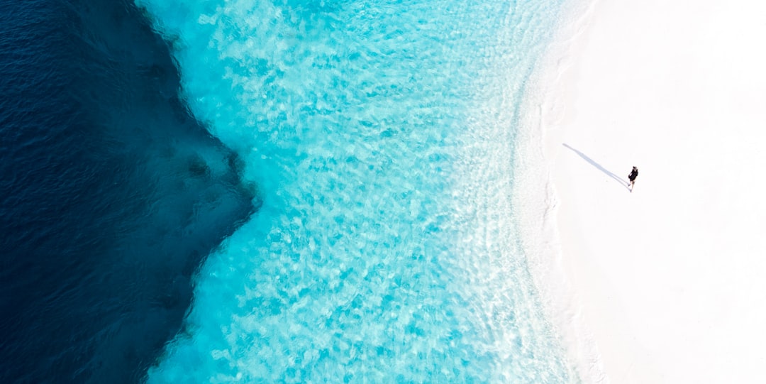 Aerial view of woman walking on white sand beach in the Maldives, blue water, drone photography, wide angle lens, top down perspective, minimalist composition, minimalism, soft light, high resolution, sharp focus, natural colors, high contrast, clear details, pure nature, peaceful atmosphere, turquoise color –ar 2:1