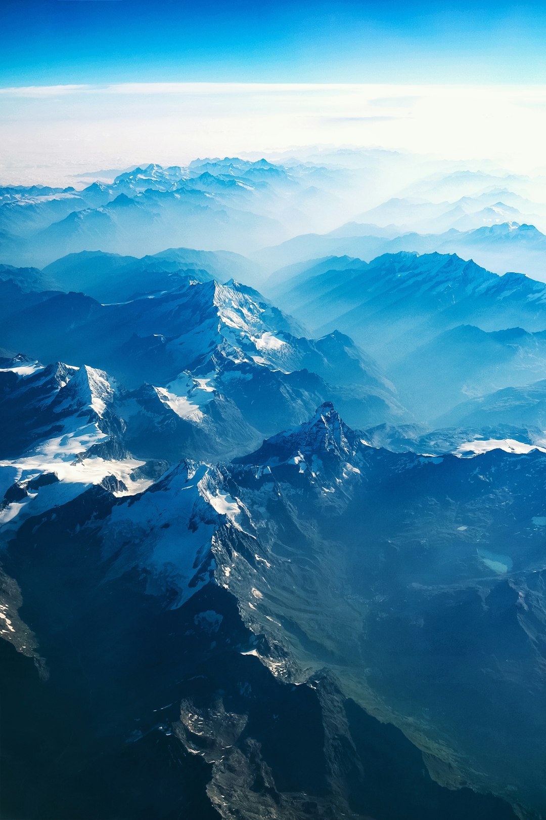 Aerial view of the Alps, snowcapped mountains in blue tones, beautiful nature photography, aerial photo from an airplane, clear sky, high resolution, high detail, sharp focus. The style is similar to studio lighting. –ar 85:128