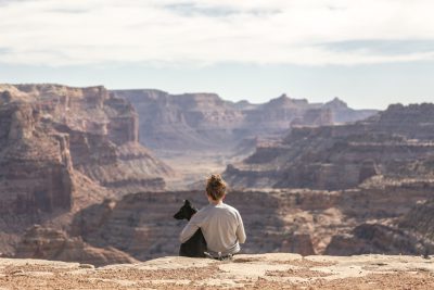 A woman sitting with her dog on the edge overlooking the Grand Canyon, shot from behind, in a white shirt and black pants, a peaceful moment, a beautiful view, taken with a Canon EOS R5 camera. --ar 128:85