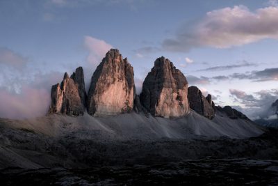 Photo of the three lavaredo peaks, shot with a Sony Alpha A7 III and an f/2 lens in sunset lighting with a black sky and grey clouds, taken from a low angle at high resolution in a hyper realistic, cinematic style. --ar 128:85