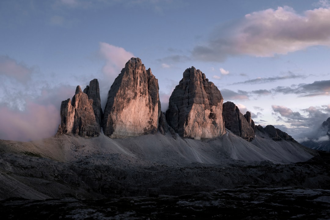 Photo of the three lavaredo peaks, shot with a Sony Alpha A7 III and an f/2 lens in sunset lighting with a black sky and grey clouds, taken from a low angle at high resolution in a hyper realistic, cinematic style. –ar 128:85