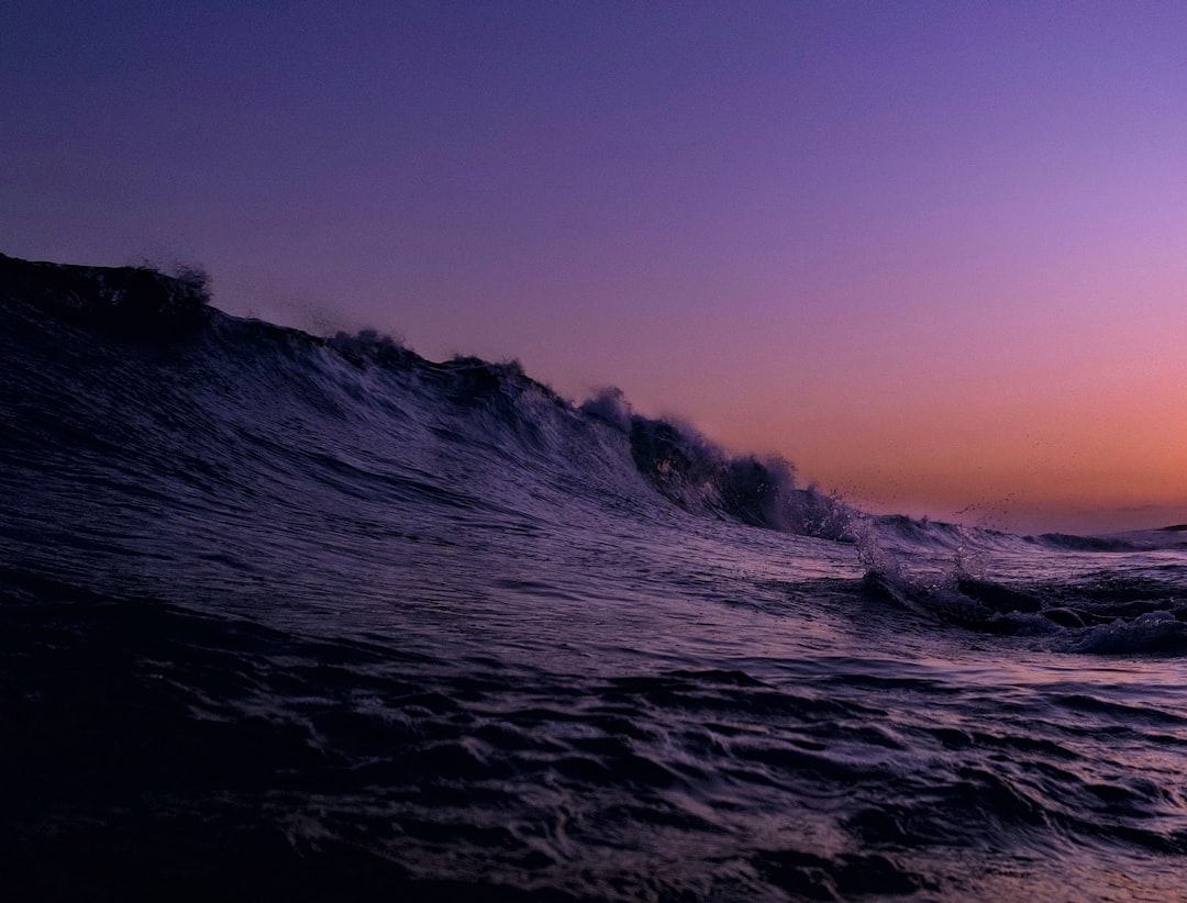 photo of ocean waves at dusk, purple sky, dark water, low angle, wide ...