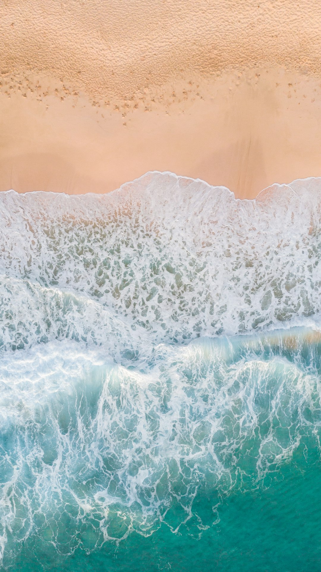 A photo of the top view of waves crashing on an Australian beach, taken from above with a drone. Beautiful sand and turquoise water, soft lighting, natural colours, high resolution, in the style of hyper realistic. –ar 71:128