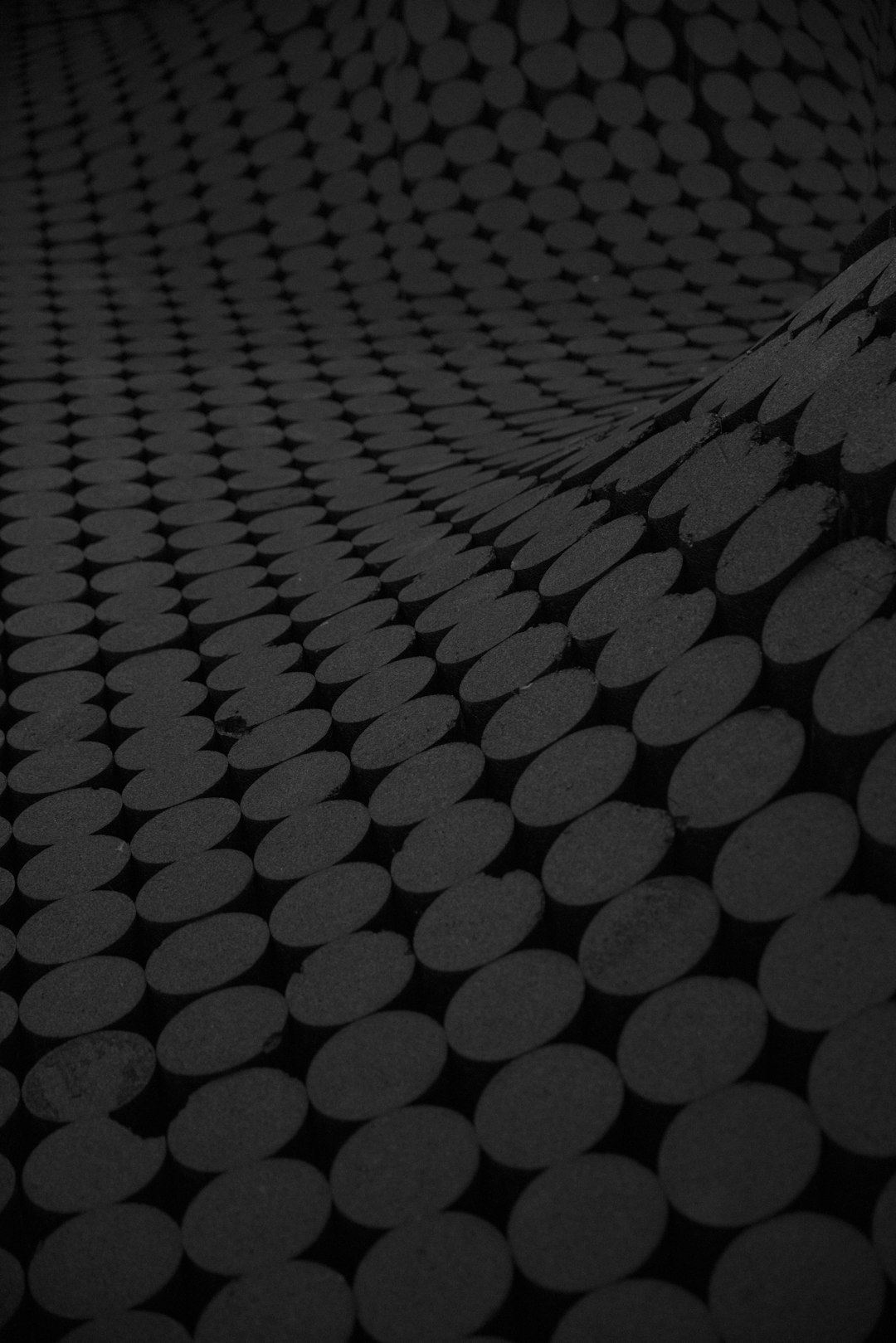 Dark gray background with black dots in the style of 3D renderings, featuring circular shapes at high resolution against a dark gray background. The overall color scheme is simple, with only one layer of light grey on top. It has an extremely low perspective, with large circles arranged at different heights to form a pattern resembling undulating hills. There are no text or other elements. –ar 85:128