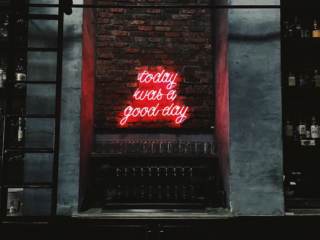 A red neon sign on the wall of an industrial bar that says “esque today was good day –ar 4:3