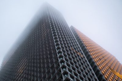 A tall building with triangular windows in the fog, modern architecture in a low angle view, high resolution photography with professional color grading, soft shadows and no contrast, clean sharp focus, digital photography using a Canon EOS R5 camera and volumetric lighting. --ar 128:85