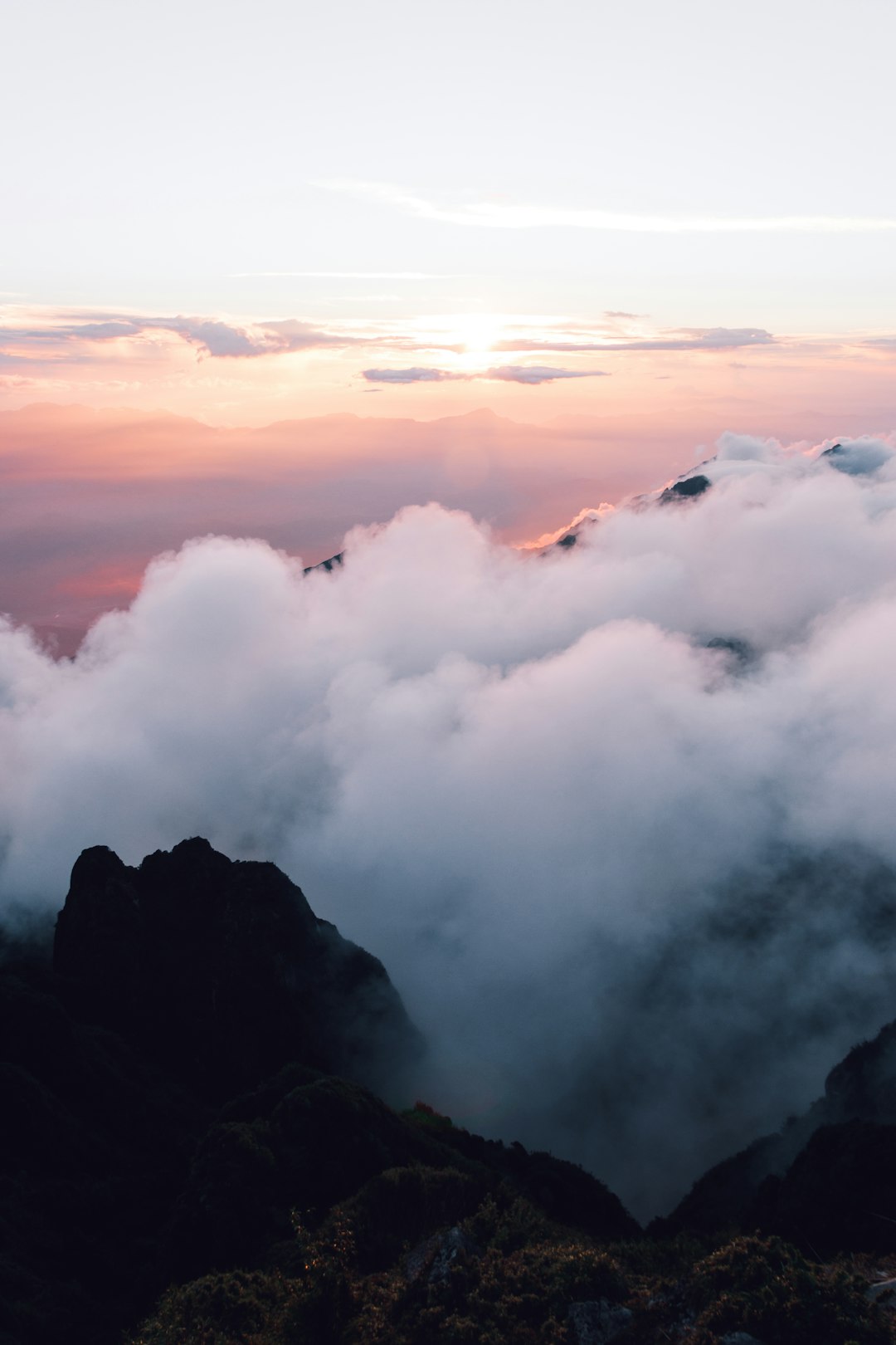 Photo of sunrise on the top of Mount Lao, with clouds rolling over mountains and hills in front of it. The sky is light pink, and there’s some mist floating above them. It was taken from an overhead perspective at high altitude, showing the magnificent scenery of nature. This photo conveys emotions through light colors, showcasing spectacular natural landscapes. Soft tones create a peaceful atmosphere, giving people tranquility.,,in –ar 85:128