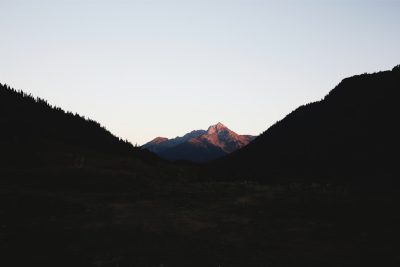 Photograph of the silhouette mountains at dusk, in British Columbia Canada, near Whistler with trees and light pink mountain peaks against a black sky in the evening light. The image is clear, beautiful, simple, clean and minimal. --ar 128:85