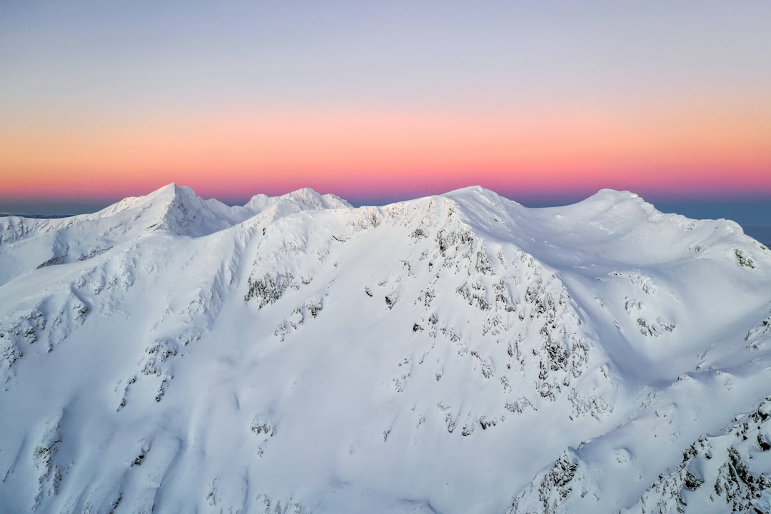 Aerial view of snow-covered mountains at sunrise, pink and purple sky, Sony A7R IV with panoramic lens, high resolution for crisp details, in the style of aerial photography, snowcapped peaks. –ar 128:85