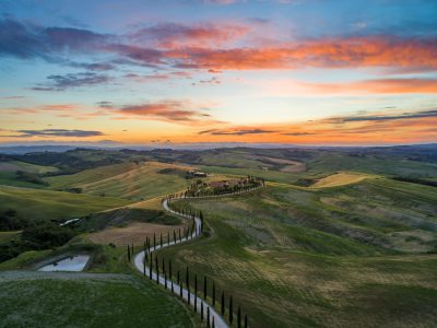 Tuscany, sunset, rolling hills and cypress trees in the foreground, a winding road leading to an old farm house, a beautiful sky with hues of orange, pink and blue, landscape photography, drone shot, rule of thirds, wide angle lens, f/20, in the style of [Ansel Adams](https://goo.gl/search?artist%20Ansel%20Adams). --ar 4:3