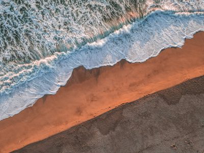 Aerial view of the sandy beach with crashing waves, captured in golden hour light, creating an atmosphere of tranquility and serenity. The contrast between warm sand tones and cool ocean hues adds depth to the scene. This aerial shot is perfect for adding a sense of vastness or solitude to your creative projects, in the style of an aerial photographer. --ar 4:3