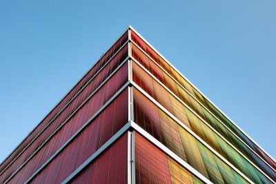 a tall building with colourful triangular metal screen on the facade, against clear blue sky, perspective view, architectural photography, architectural detail --ar 128:85