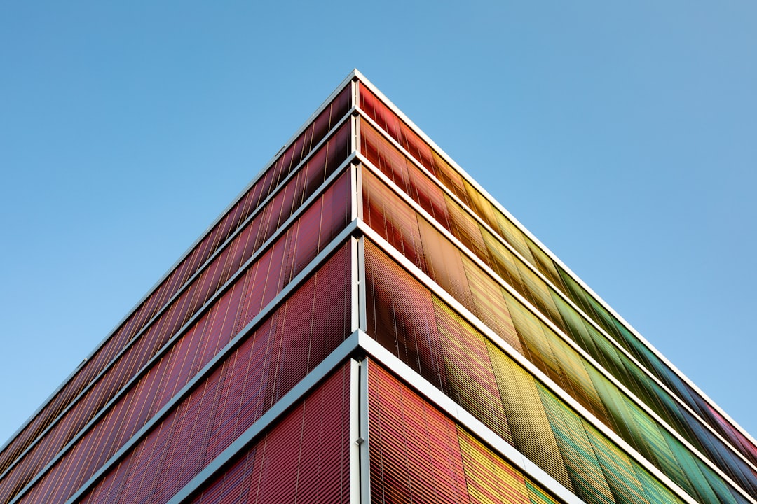 a tall building with colourful triangular metal screen on the facade, against clear blue sky, perspective view, architectural photography, architectural detail –ar 128:85