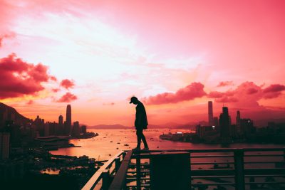 A silhouette of an urban man standing on the edge of rooftop, overlooking Hong Kong skyline at sunset, vibrant pink sky, capturing moment of solitude and contemplation, cinematic photography style, Sony Alpha A7 III with FE2485mm f/3.0 G lens, wideangle perspective. --ar 128:85