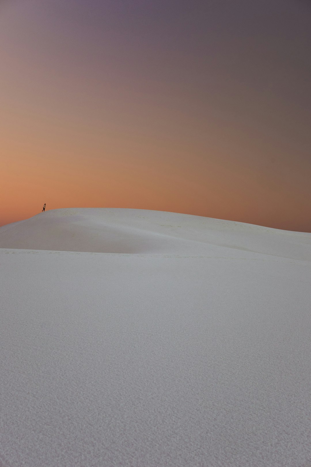 Photo of White Sand Dunes in New Mexico, white sand dune with small figure on top at dusk, orange and purple sky, minimalism, negative space, clean lines, rule of thirds. –ar 85:128